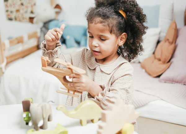 Young girl with afro hair enjoys playing with wooden toys in a cozy indoor playroom.